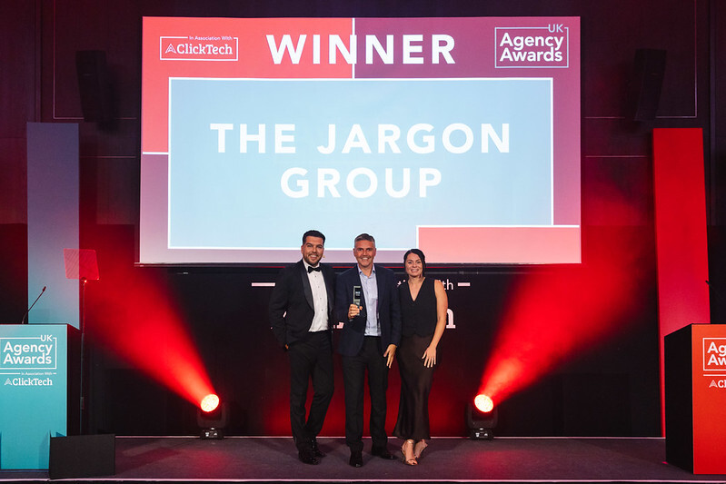 The Jargon Group representatives holding a trophy beneath their winner announcement at the UK Agency Awards