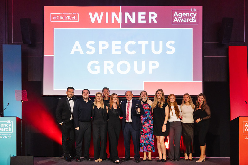 Aspectus Group team posing beneath their winner announcement at the UK Agency Awards